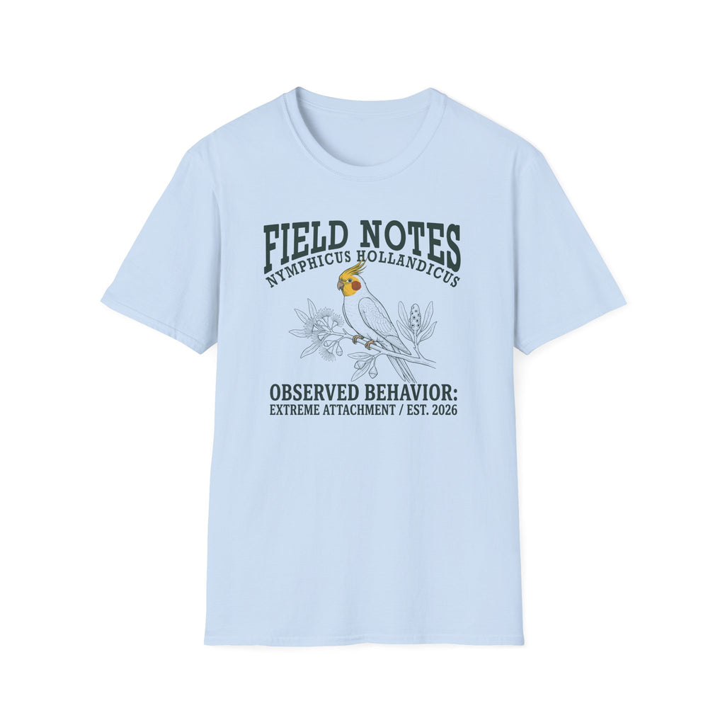 A light blue short-sleeve t-shirt with a graphic print on the front. The print features a parrot bird and the text 'FIELD NOTES', 'NYMPHICUS HOLLANDICUS', and 'OBSERVED BEHAVIOR: EXTREME ATTACHMENT / EST.