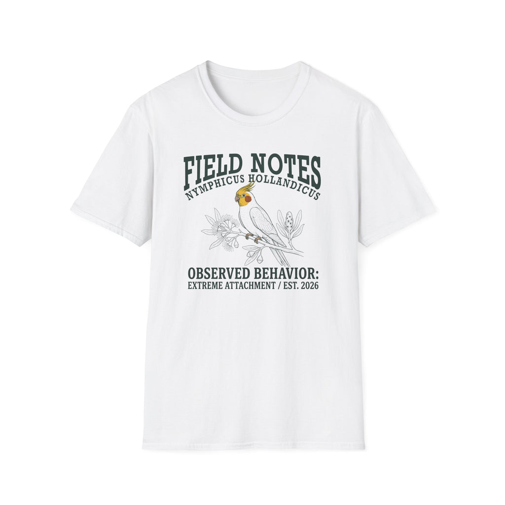 A white short-sleeve crewneck t-shirt featuring a dark green and black graphic print of a cockatel with the text 'FIELD NOTES NEMPLICUS HOLLANDICUS' and 'OBSERVED BEHAVIOR: EXTREME ATTACHMENT / EST. 2026'.
